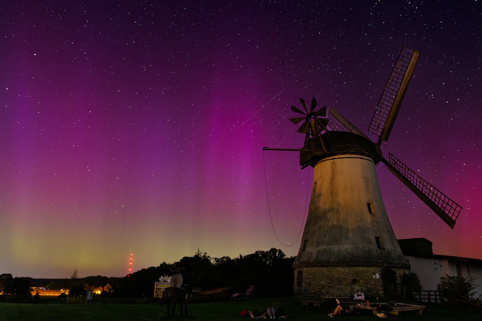 A windmill in the middle of a field with the aurora lights in the background